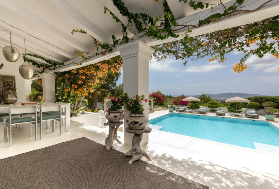 The shaded terrace by the pool, laden with flowers, at Villa El Zafiro, Ibiza. A stunning spot to take in the view while dining on a luxury self catered villa holiday in the Balearic Islands.