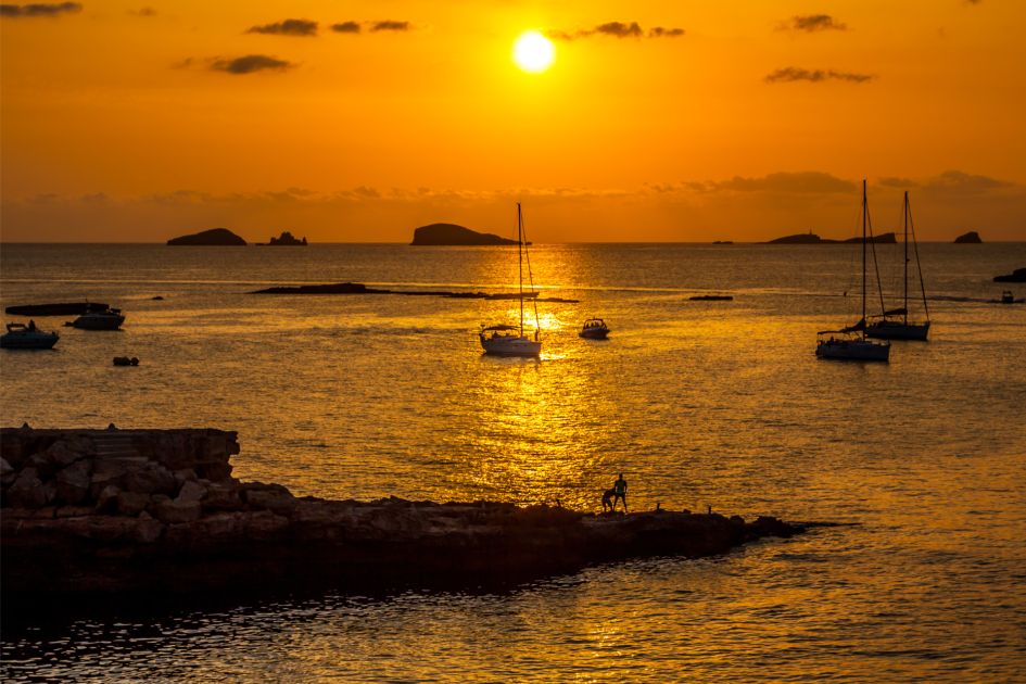 Sunset over the waters of Cala Conta beach in Ibiza, with boats in the background. 