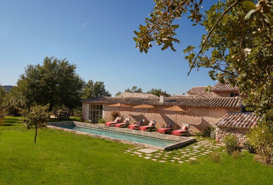 View of the externals of Le Mas Vermentino, with the swimming pool, sun loungers and parasols in the foreground. This is a lovely private luxury villa in Provence.