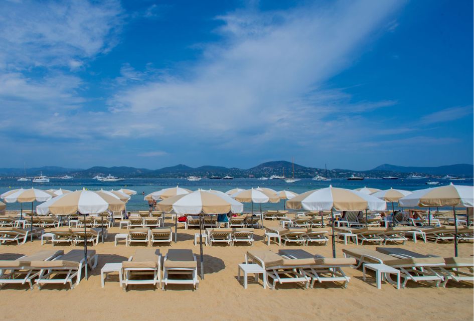 Sun loungers on Bouillabaisse Beach with views of the ocean and luxury yachts before the hilly coastline of St Tropez