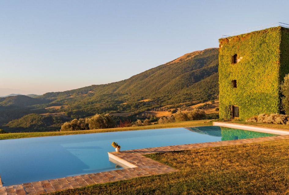 The luxury swimming pool at Villa Torre, overlooking the rolling hills of Umbria, with a building to the side adorned with lush green vines.